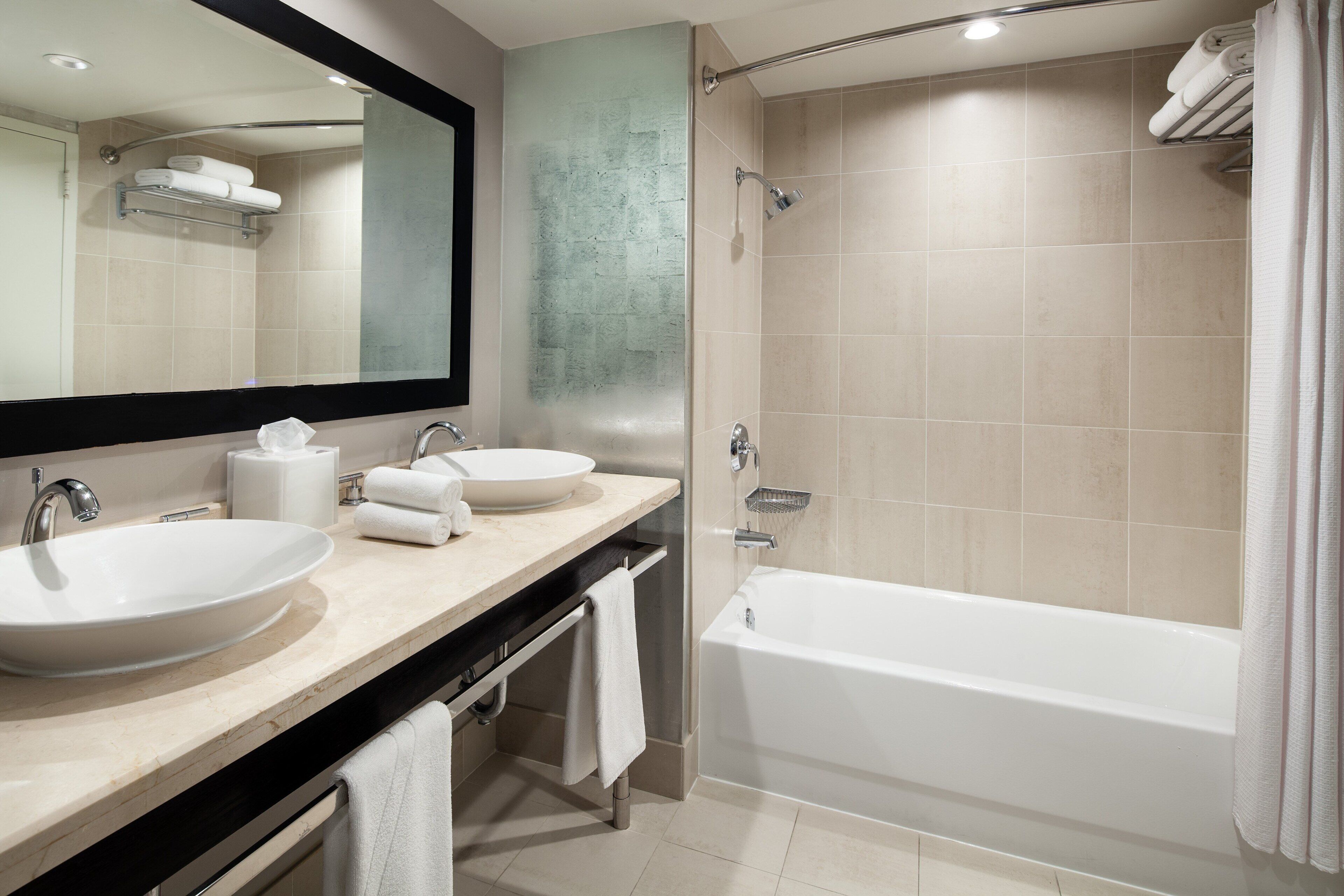 A modern bathroom with two sinks, a large mirror, a bathtub, and a shower area.