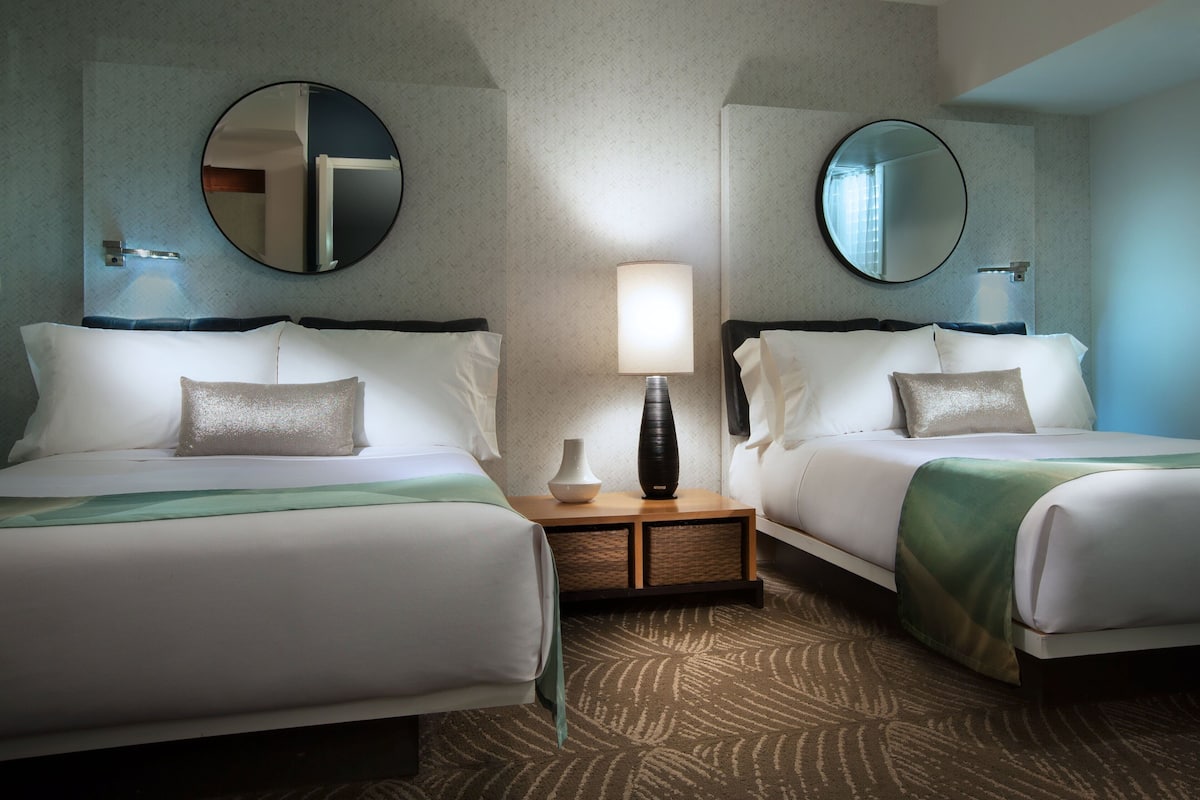 Une chambre d’hôtel avec deux lits, une table de chevet avec une lampe et deux miroirs fixés au mur.