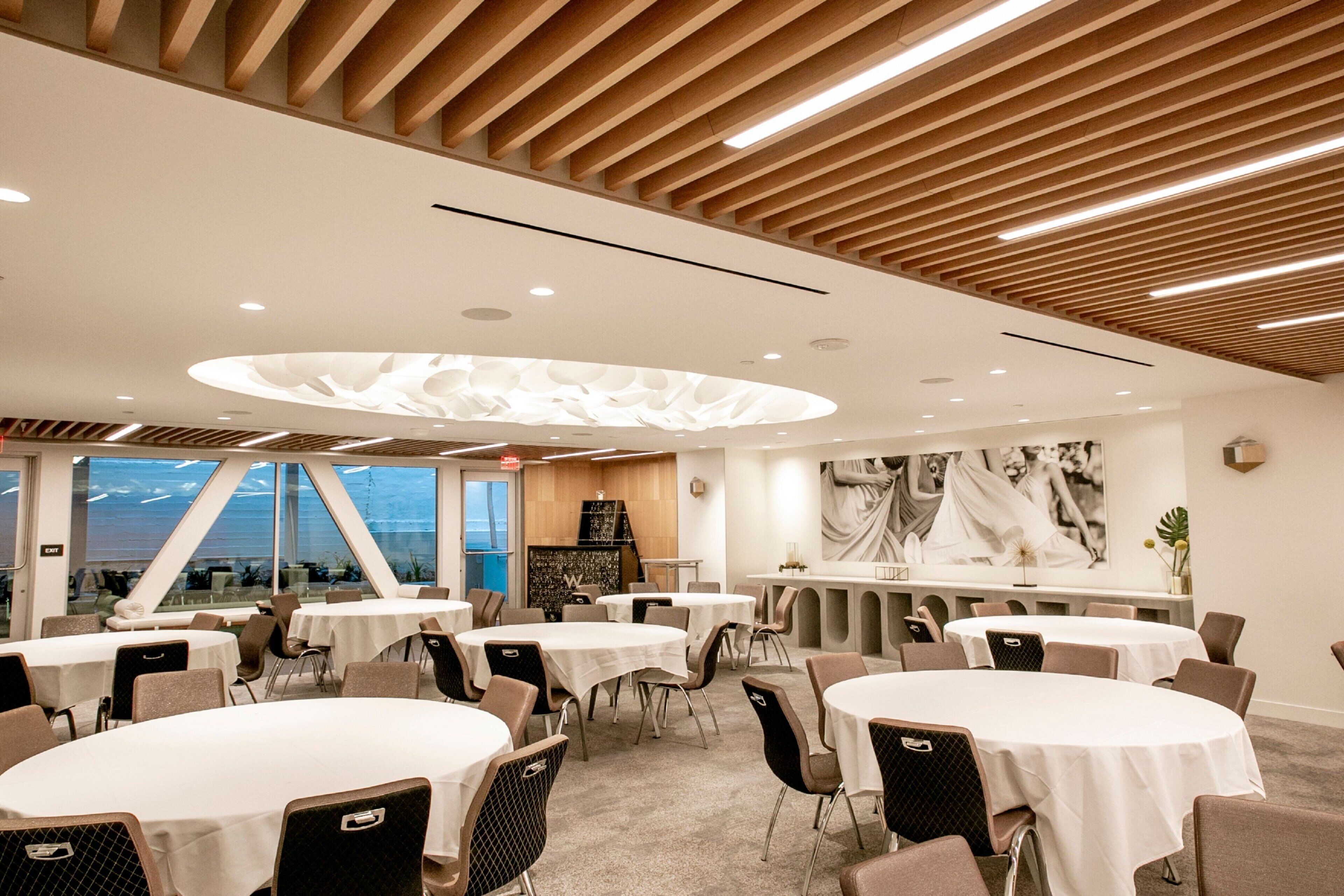 A modern hotel dining area with round tables, chairs, and a wooden ceiling.