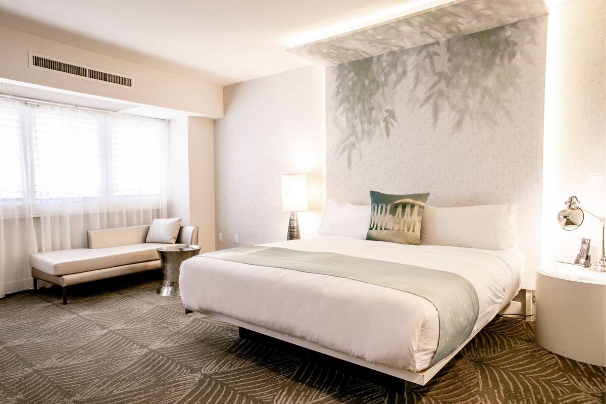 Une chambre d’hôtel avec un grand lit, un canapé, une table de chevet et une lampe fixée au mur.
