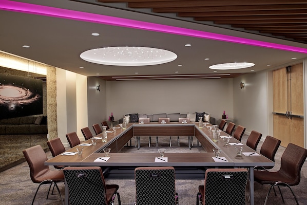 A conference room with a long table, multiple chairs, and a large screen displaying a galaxy image.