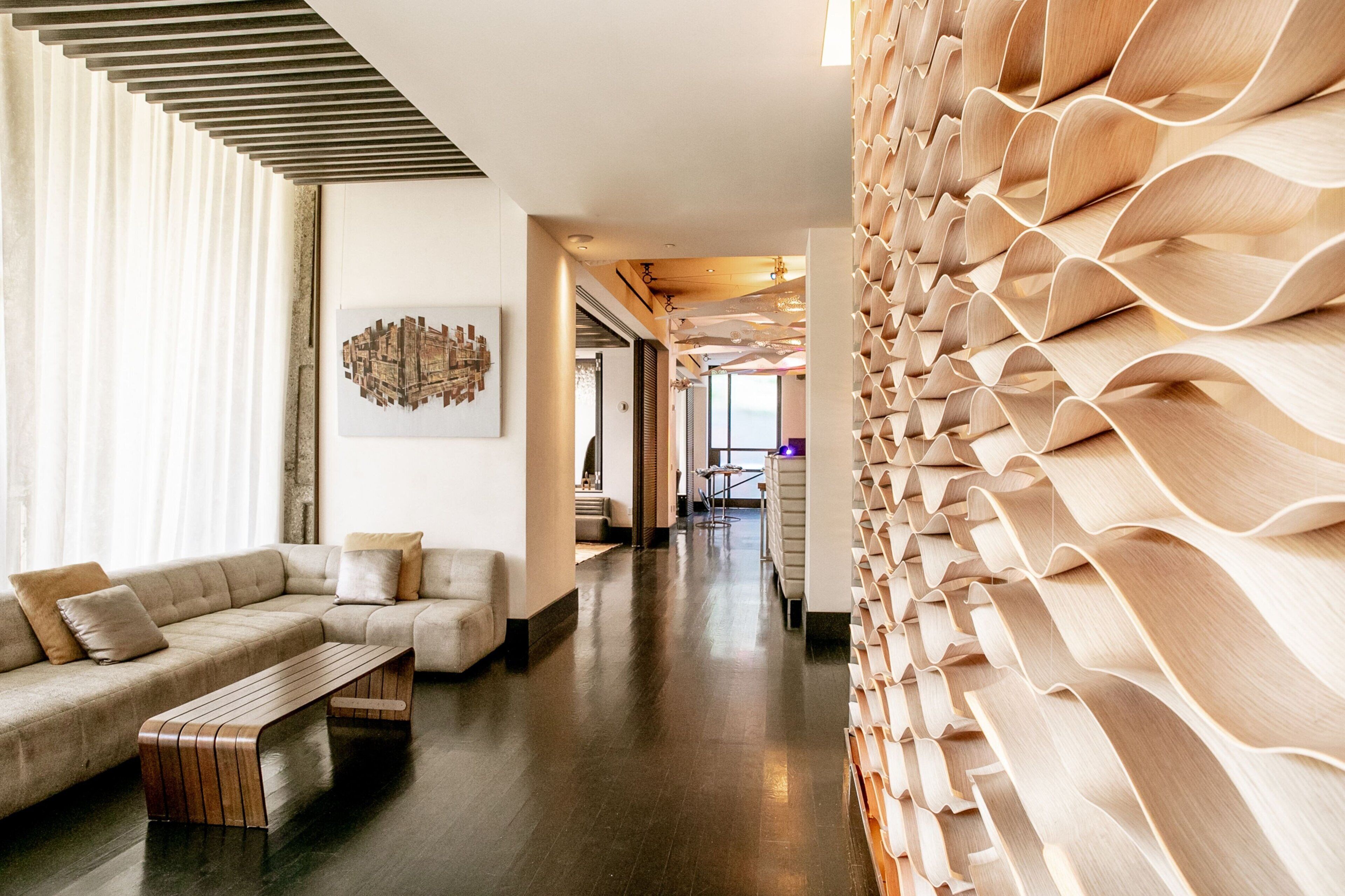 Un intérieur moderne avec un canapé d’angle, un banc en bois et un élément décoratif mural en bois original.