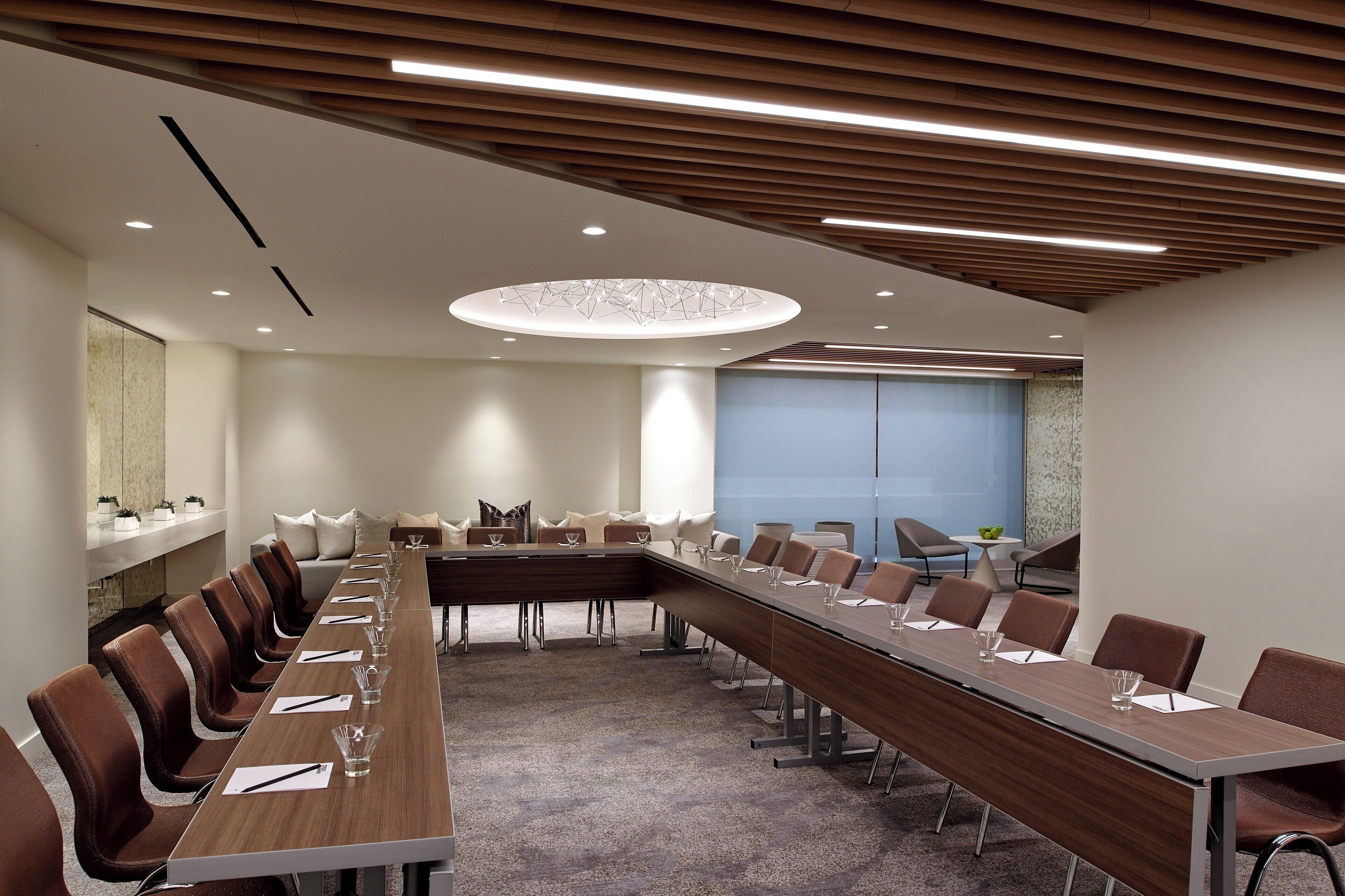 Une salle de conférence dotée d’une longue table, de chaises marron et d’un plafond au design moderne.