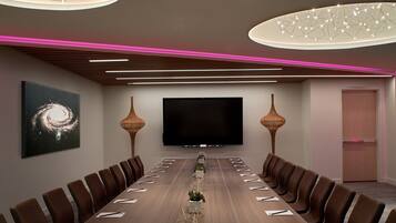 A conference room with a long table, brown chairs, a flat-screen TV, and modern lighting fixtures.