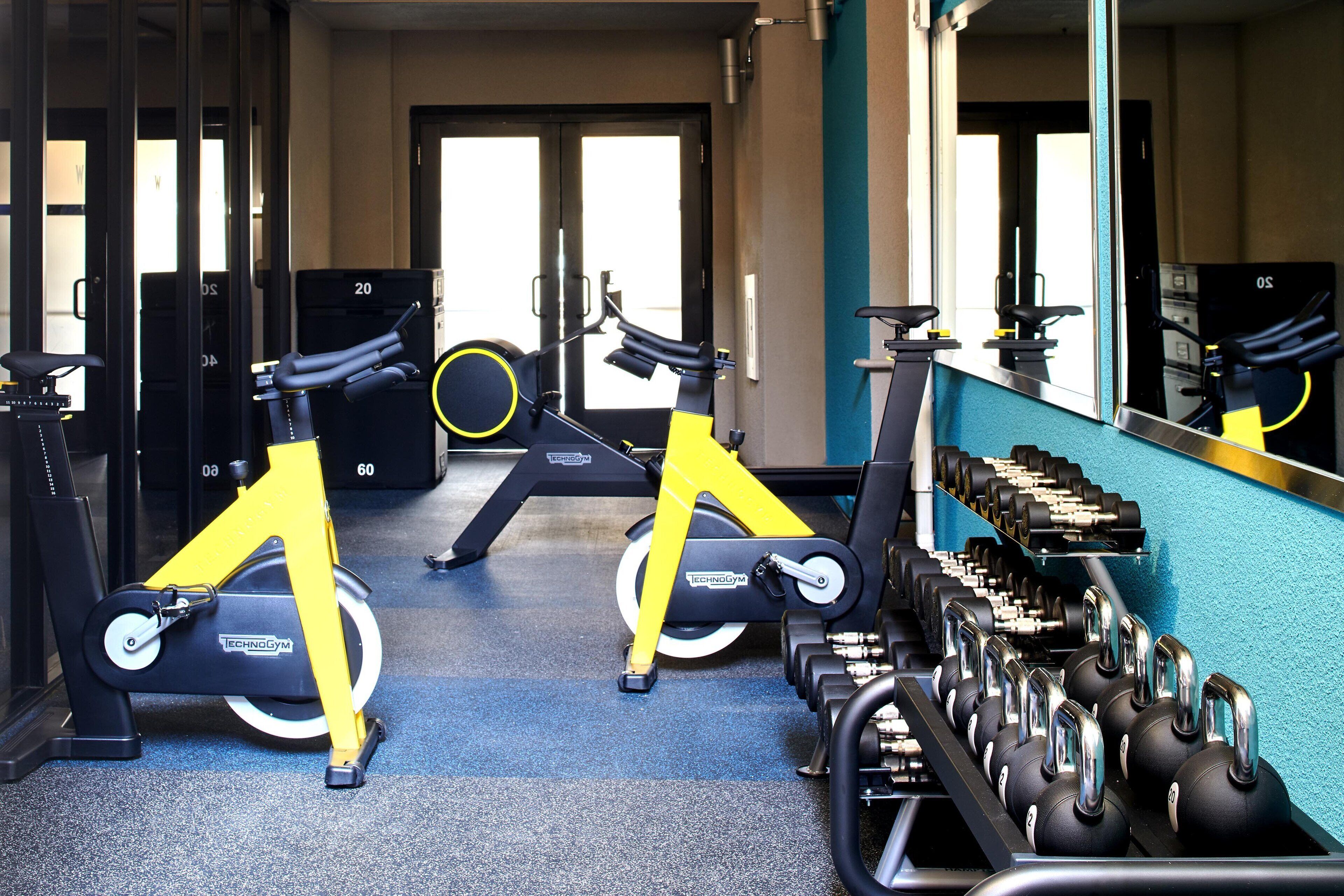 A gym with stationary bikes, dumbbells, and a mirror reflecting the equipment.