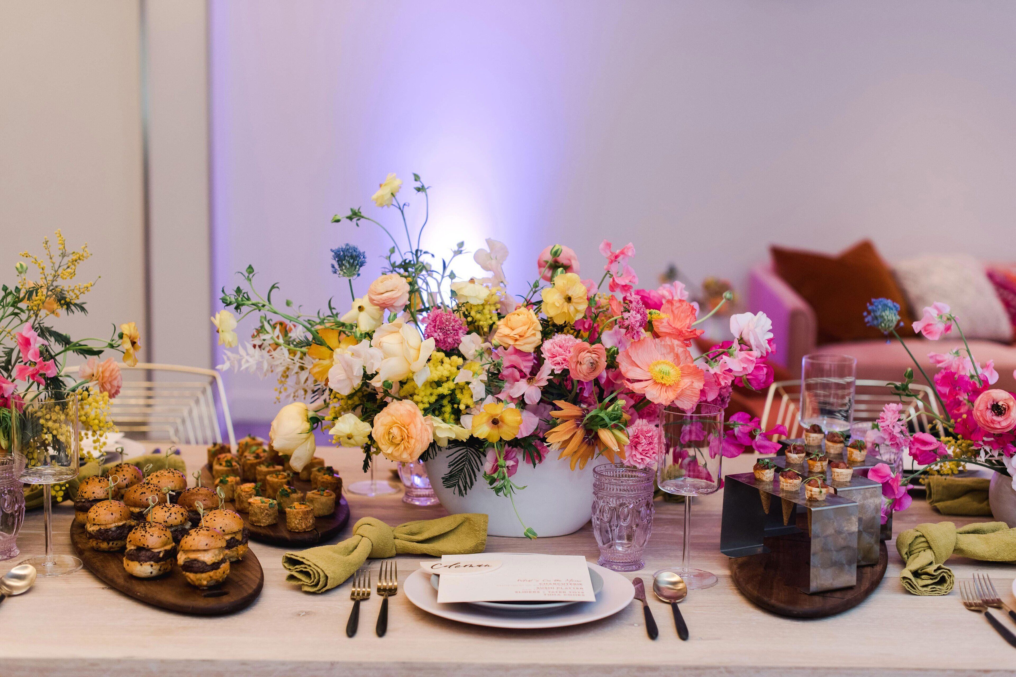 A table set with food, drinks, and a floral centerpiece.