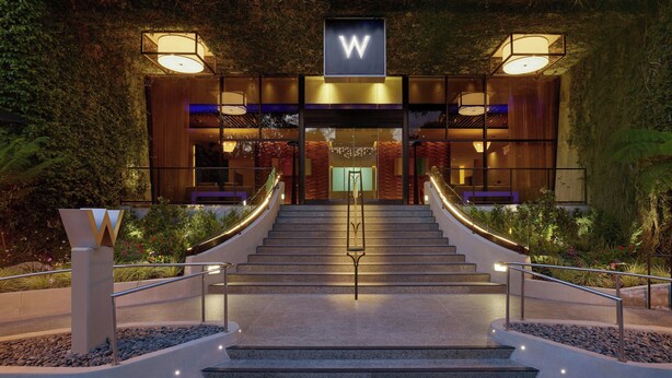 Een moderne hotelentree met een opvallend 'W'-bord, een trap die naar de lobby leidt, en een goed verlichte gevel.