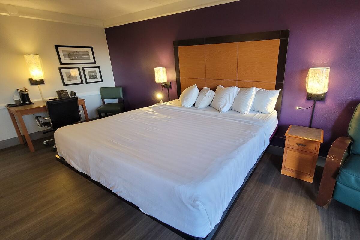 A hotel room with a large bed, a desk, a chair, and two wall-mounted lamps.
