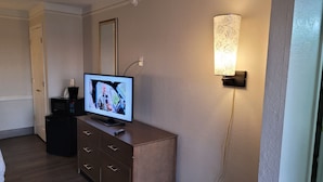 Een hotelkamer met een flatscreen televisie op een houten dressoir, een wandlamp en een deur met een spiegel.