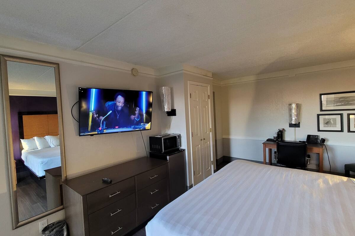 A hotel room with a large bed, a TV mounted on the wall, a desk with a computer, and a microwave.
