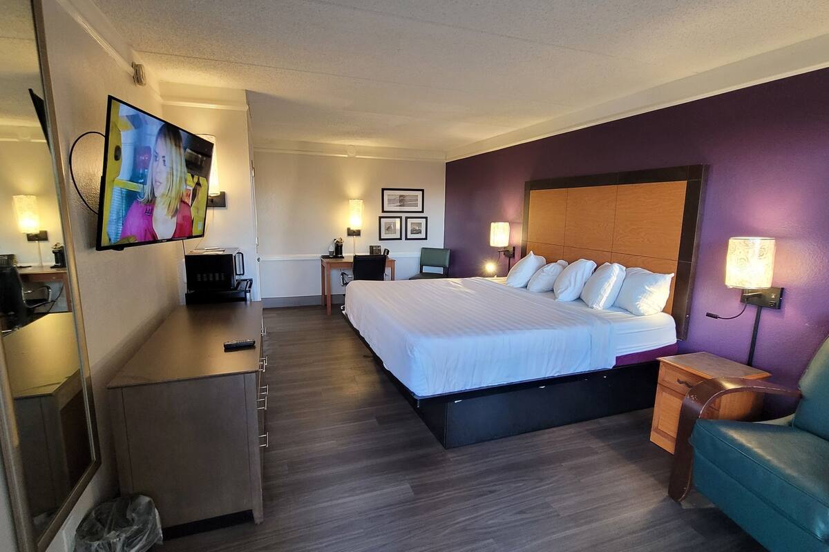 A hotel room with a large bed, a desk, a chair, and a TV.