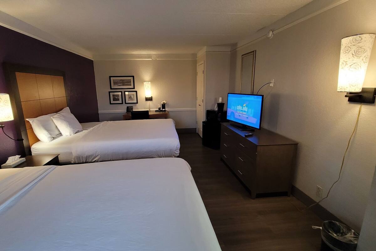 A hotel room with two beds, a television, a desk, and a trash bin.