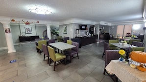 Een restaurant met een bar, meerdere tafels en stoelen, en een betegelde vloer.