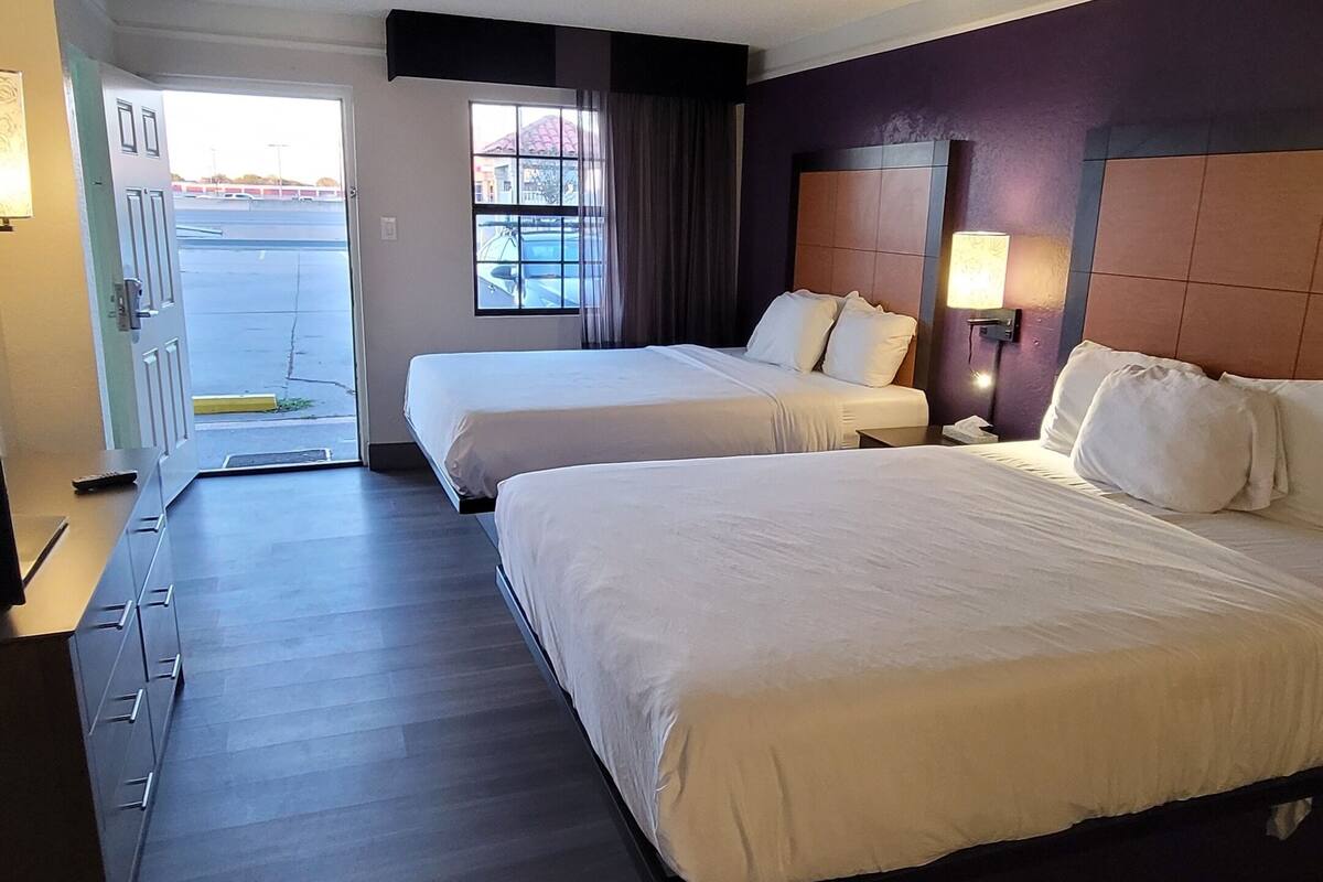A hotel room with two beds, a desk, and a window with a view of the parking lot.
