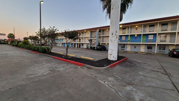 A parking lot with a row of multi-story buildings, some with balconies and a few with green doors.