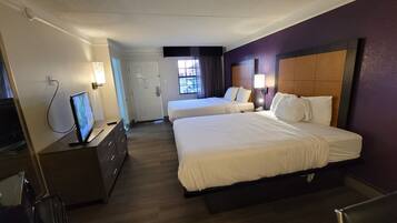 A hotel room with two beds, a TV, a dresser, and a window with curtains.