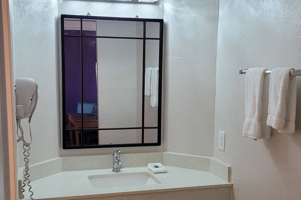 A bathroom with a large mirror, a sink, and a towel rack.
