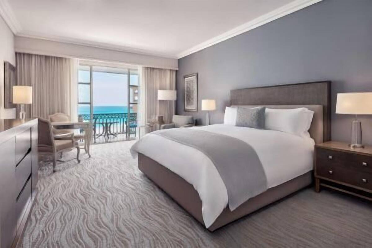Une chambre d’hôtel avec un grand lit, un bureau et une chaise, un balcon avec vue et une grande fenêtre.