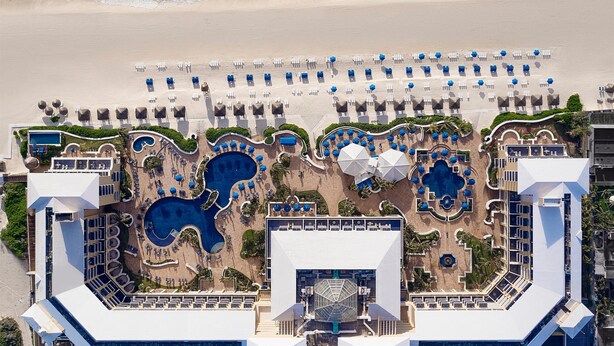 Vista aérea de un resort con varias piscinas, zonas de descanso en la playa y acceso directo a la costa.