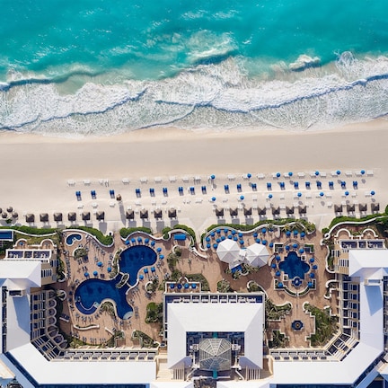 An aerial view of a resort with multiple swimming pools, beachside lounge areas, and a beachfront.