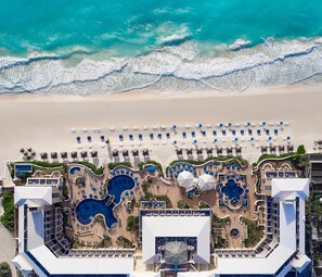 Une vue aérienne d’un complexe hôtelier doté de plusieurs piscines, d’espaces de détente au bord de la plage et d’un accès direct à la plage.