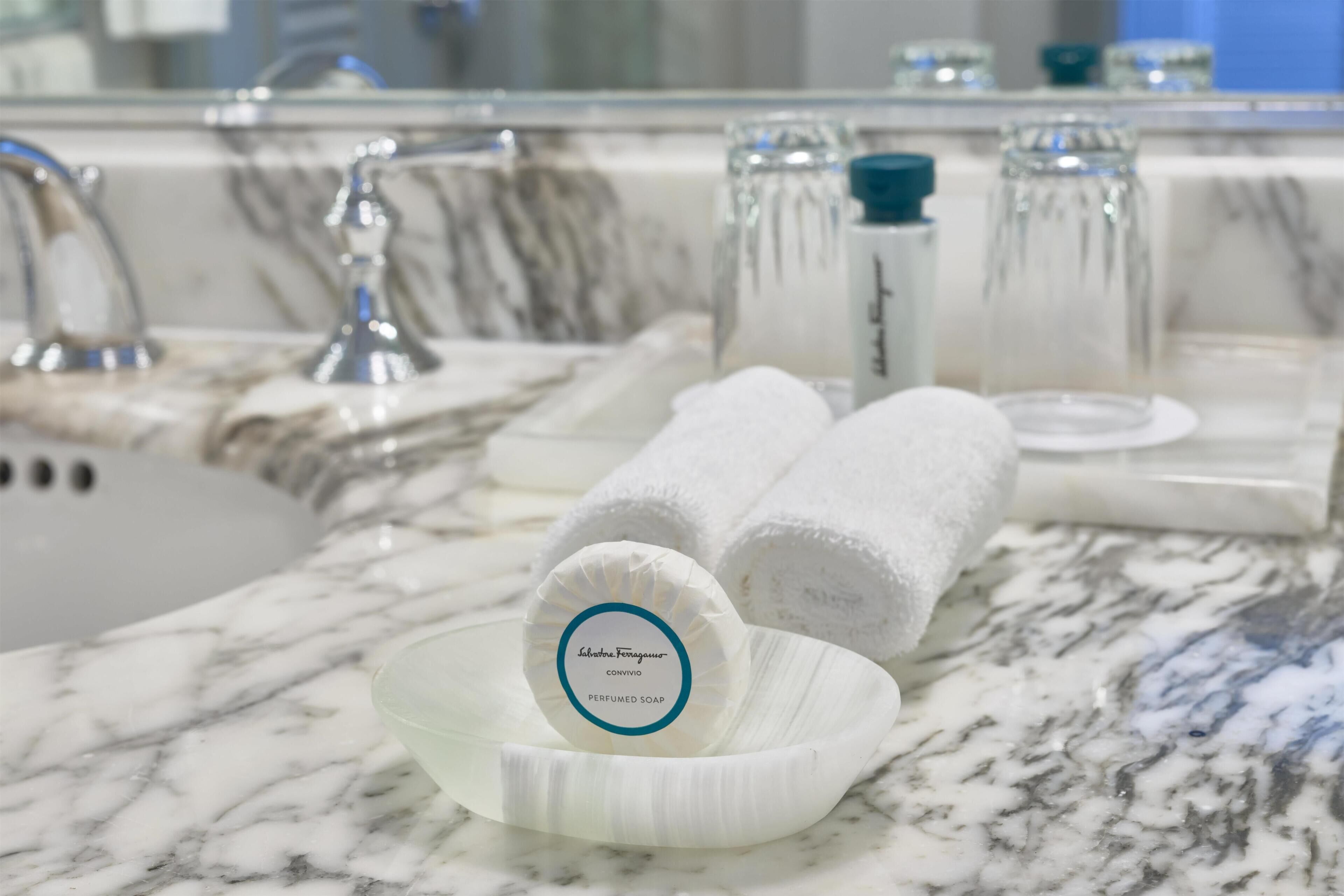 Une salle de bain dotée d’un comptoir en marbre, d’un lavabo, d’un miroir et de produits de toilette, notamment un porte-savon contenant un savon.