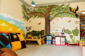 A child's playroom with a mural of a tree, toys, and a play kitchen.