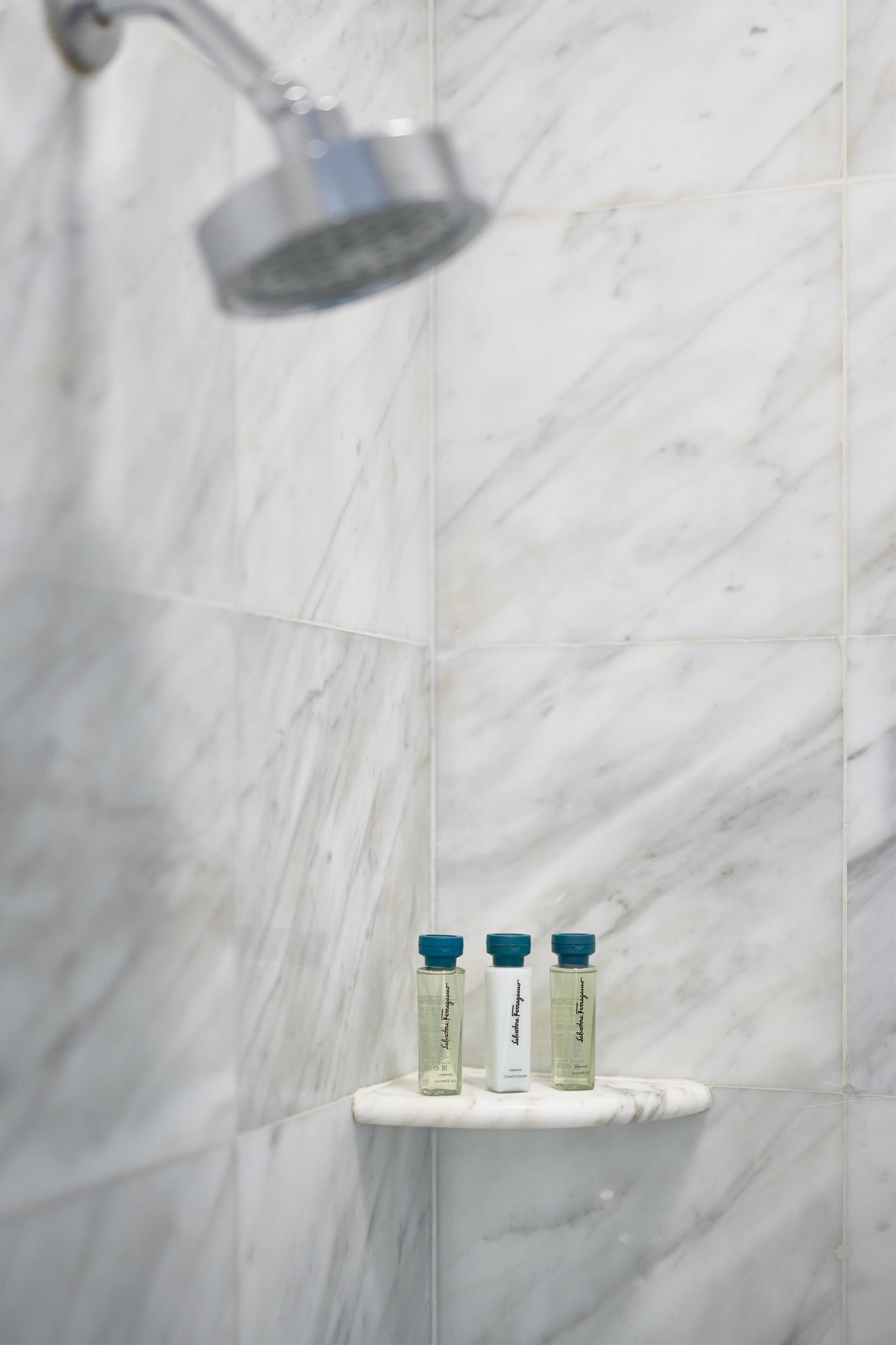 Une salle de bain avec une douche, des murs en marbre et une étagère sur laquelle sont posées trois bouteilles.