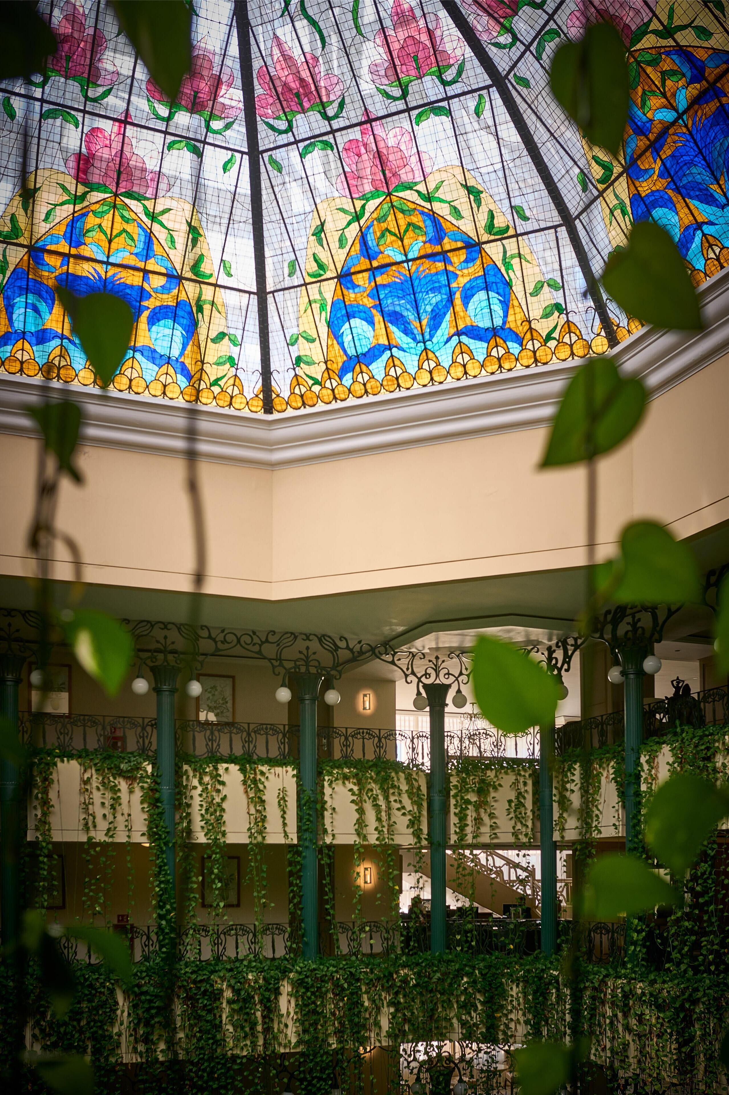 A covered atrium with a stained glass ceiling, green columns, and ivy-covered walls.