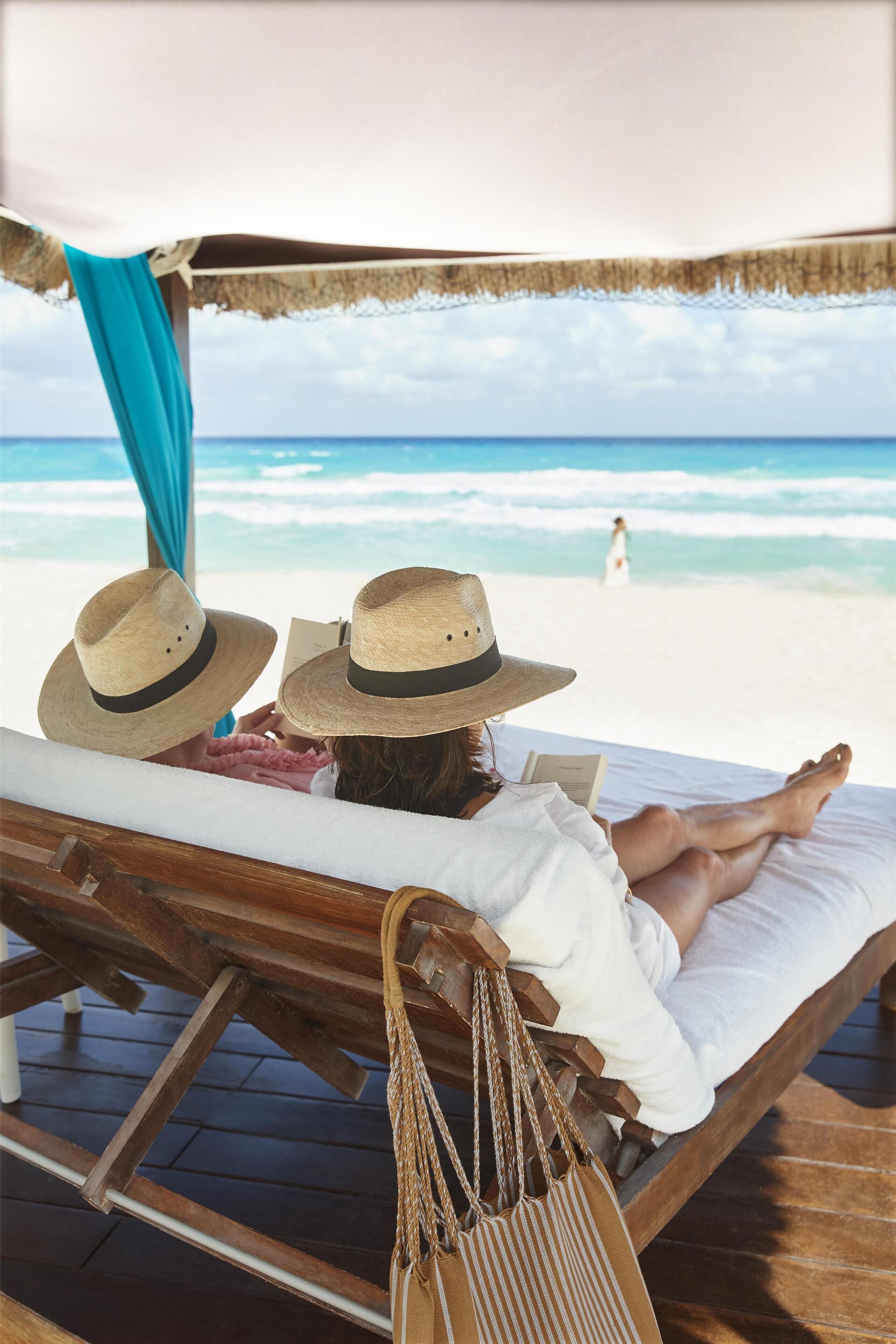 A wooden lounge chair with a white cushion, a straw hat, and a striped bag.