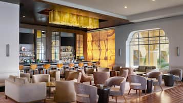 A spacious lobby with a bar area, comfortable seating, and large windows offering views of the outdoors.