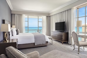 A hotel room with a large bed, a TV, a desk, and a view of the ocean.