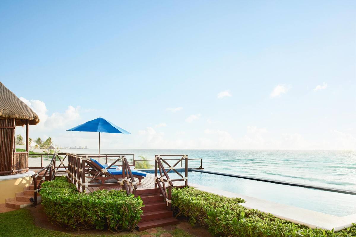 Un espace aménagé au bord de la piscine, avec des chaises longues et un parasol bleu, d’où l’on a une vue sur l’océan.
