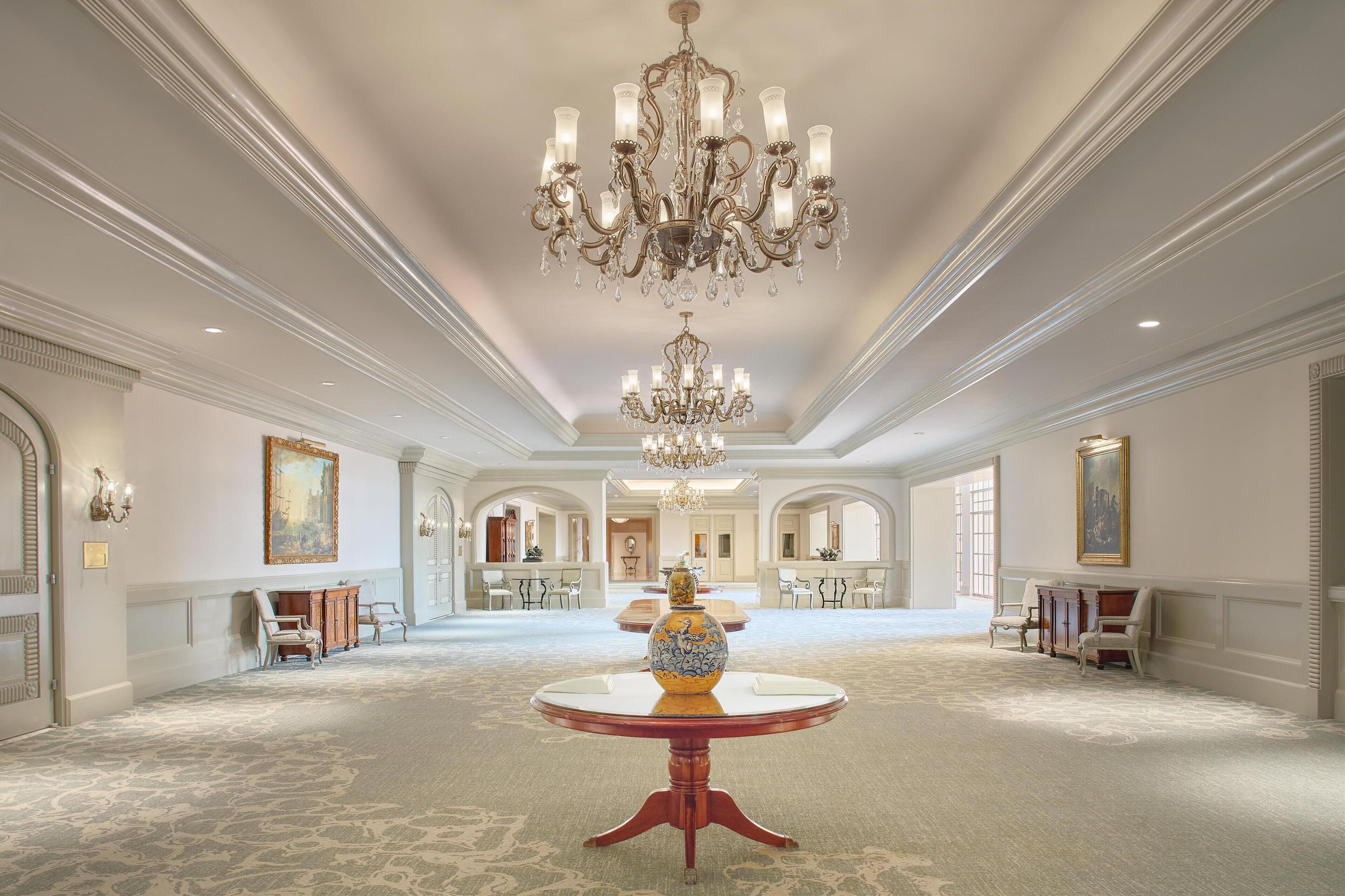 A grand hall with a large chandelier, ornate ceiling, and a central table with a vase.