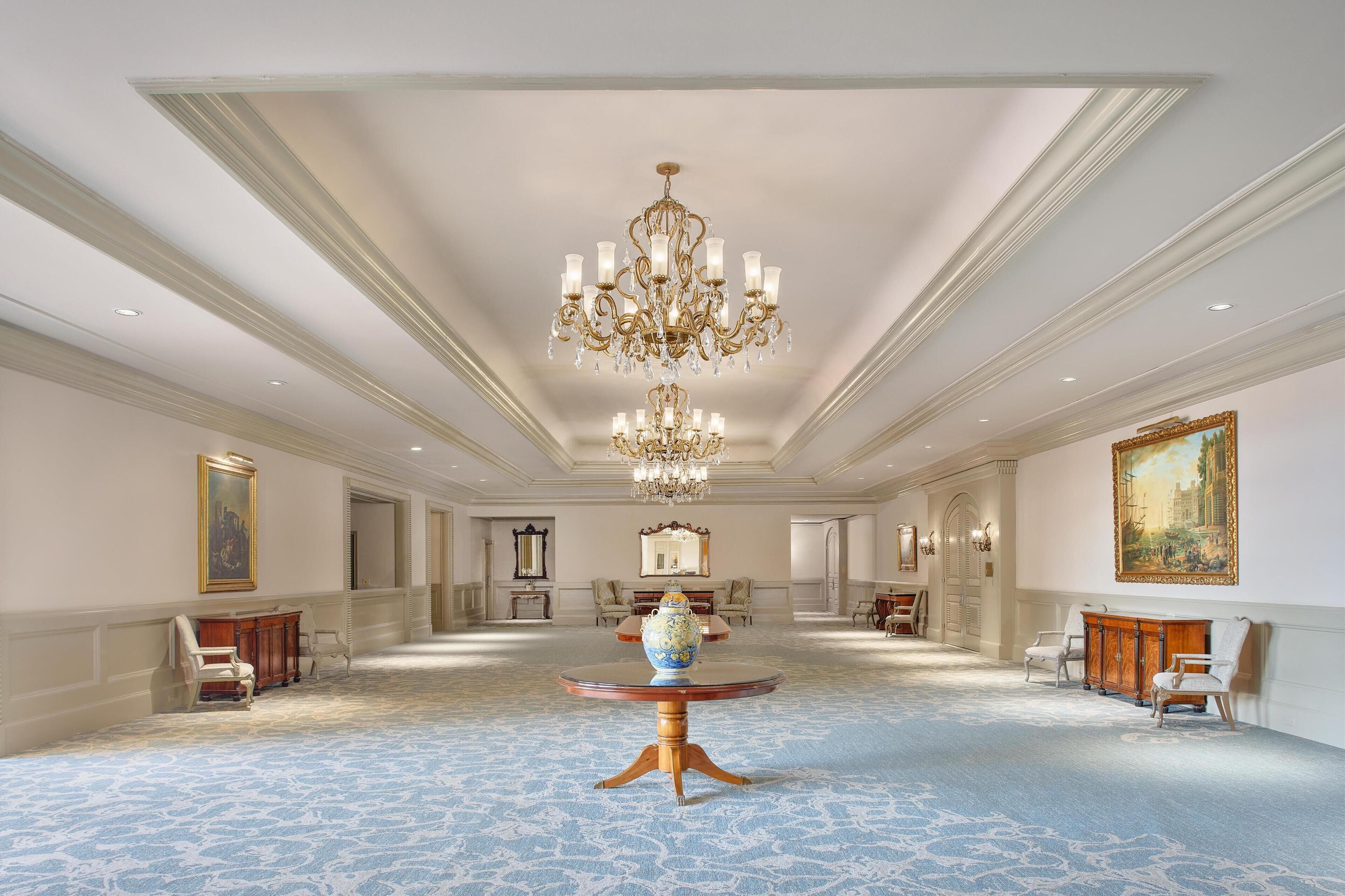 Une pièce spacieuse et élégamment décorée, avec un grand lustre, une table ronde ornée d’un vase et plusieurs chaises.
