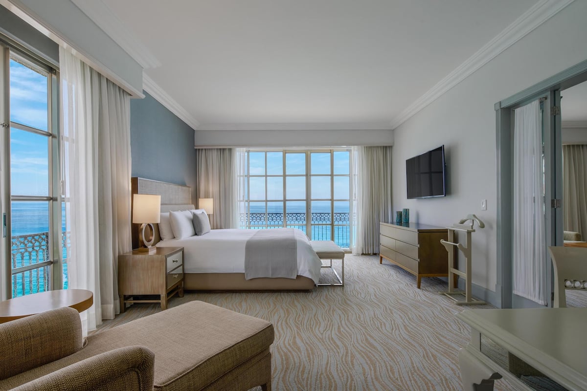 Une chambre d’hôtel avec un grand lit, un bureau, une chaise, une télévision et une vue sur l’océan.