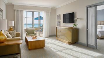 A hotel room with a view of the sea, a sofa, a coffee table, a TV, and a bed.