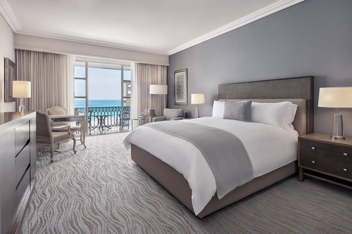 Une chambre d’hôtel moderne dotée d’un grand lit, d’un bureau et d’un balcon offrant une vue sur l’océan.
