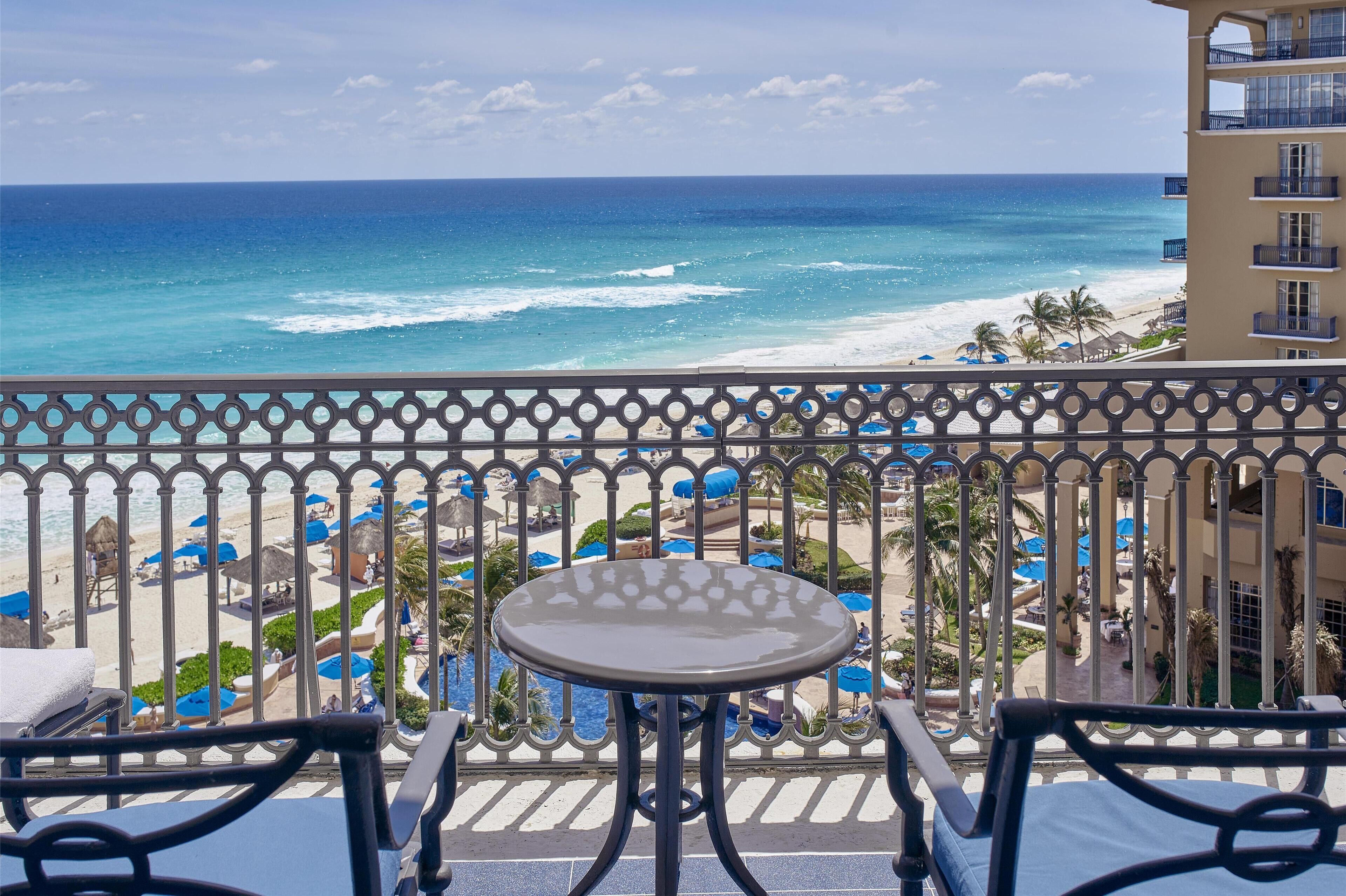 Un balcón con vista al océano y la playa, que incluye una mesa y sillas.