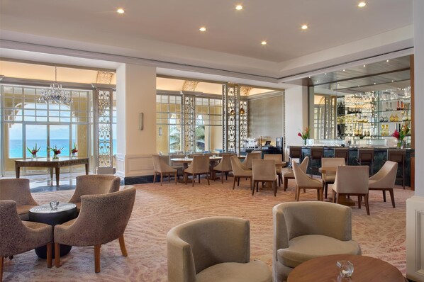 Un vestíbulo amplio con zona de bar, asientos y ventanas grandes con vistas al mar.