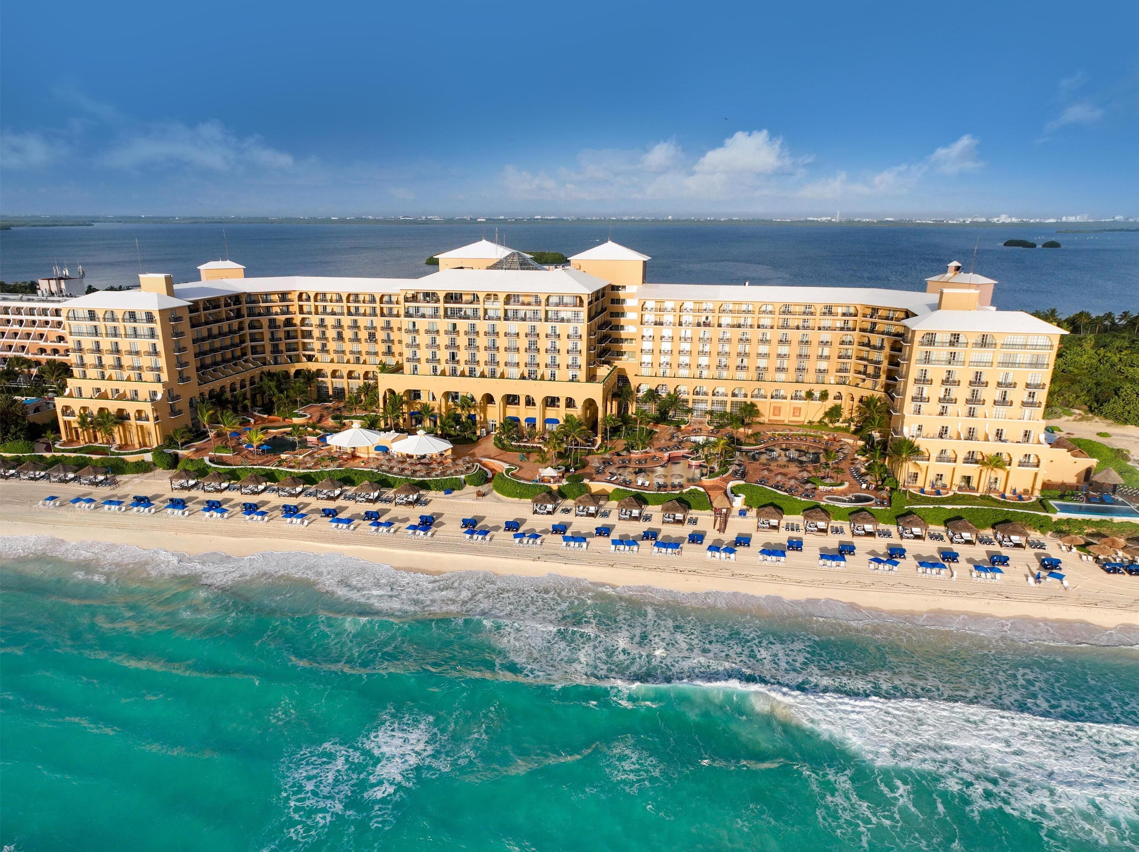 A large resort with multiple buildings, a beach with sun loungers, and a view of the ocean.