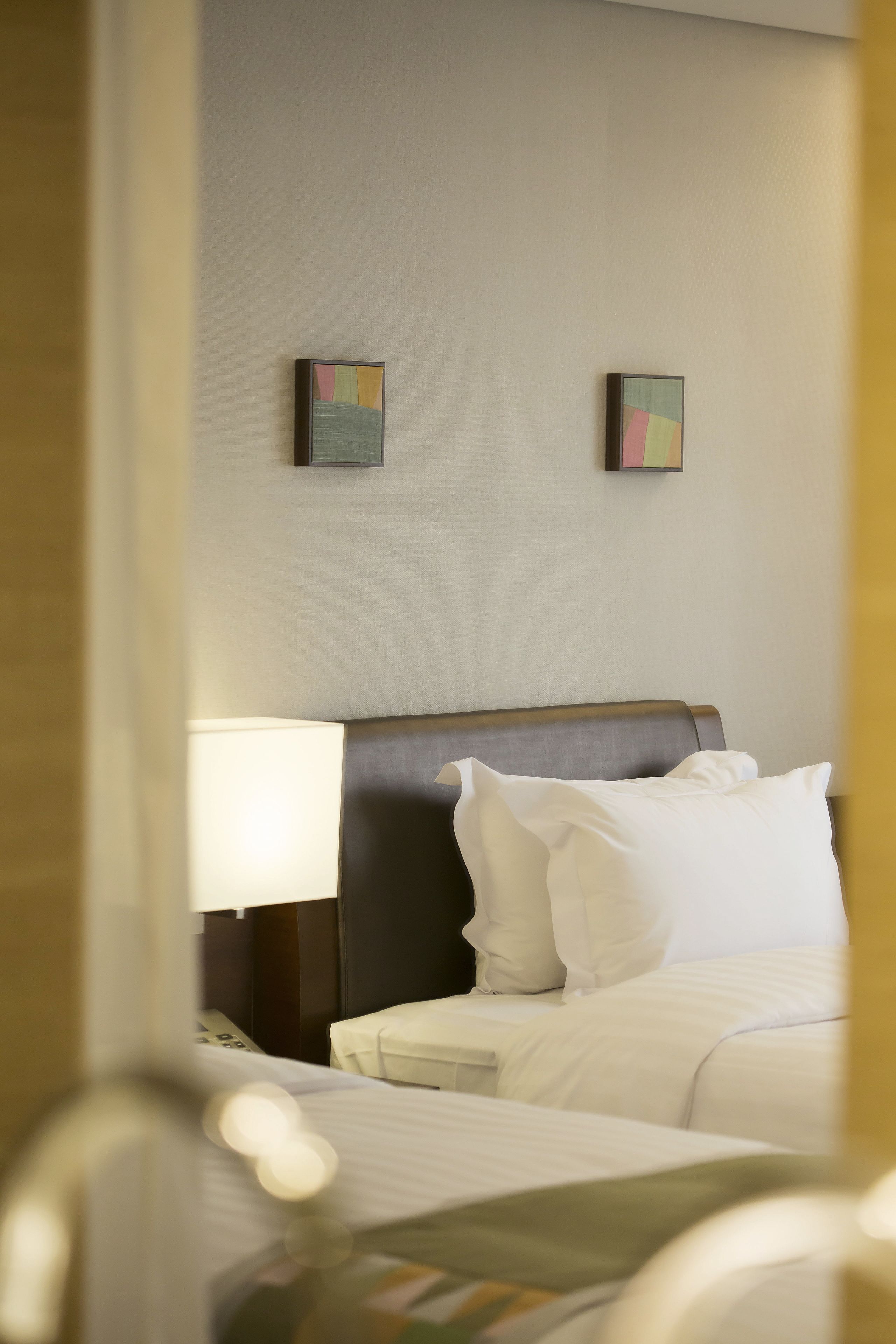 A hotel room with a bed, a bedside table, a lamp, and two wall-mounted paintings.
