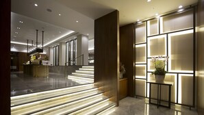 Un moderno vestíbulo de hotel con una escalera iluminada por luces LED, un mostrador de recepción y una planta en maceta.