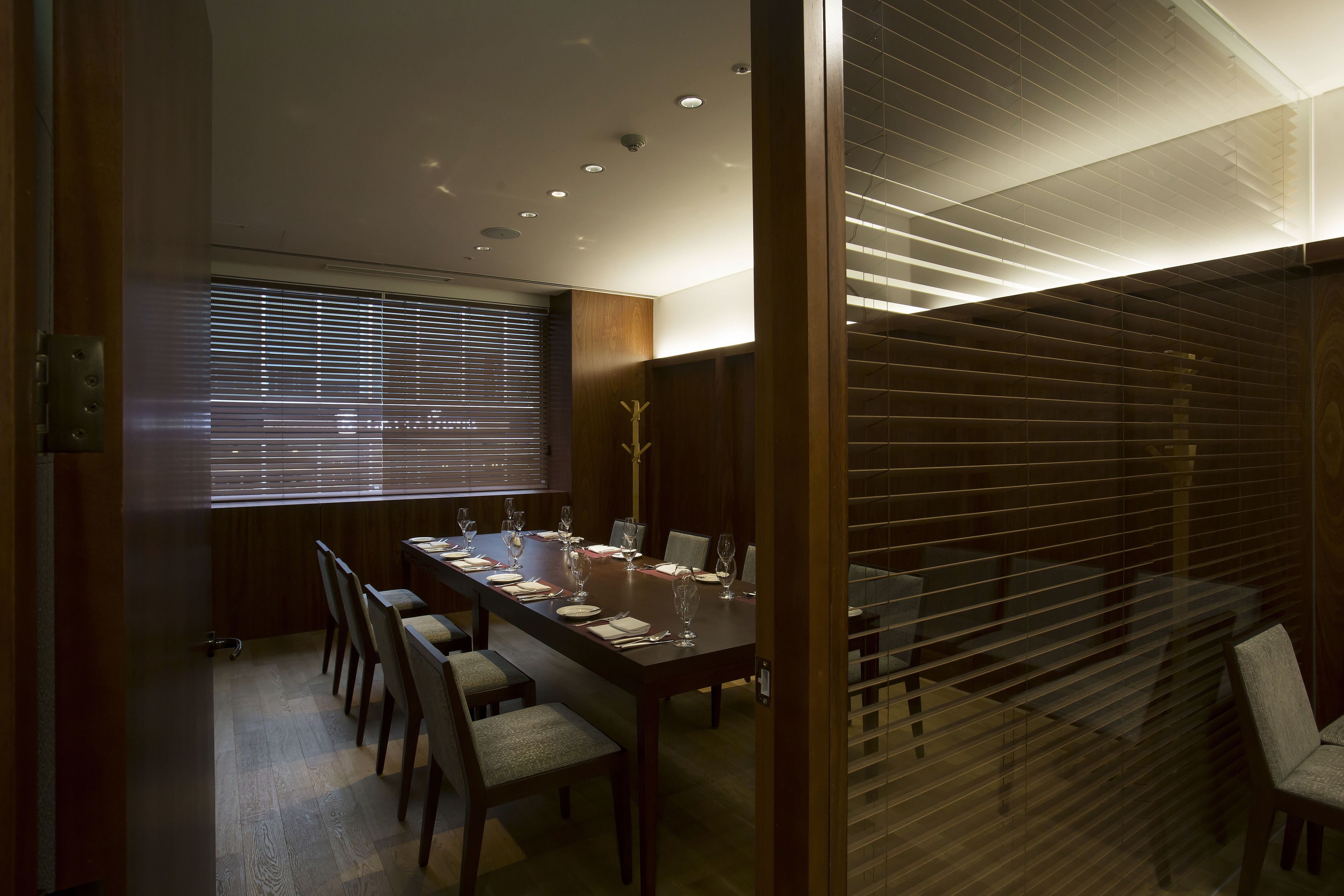 A dining area with a long table set for six, wooden chairs, and a window with blinds.