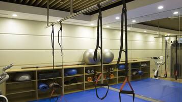 Un gimnasio con equipo de yoga aéreo colgante, pelotas de ejercicios y una zona de colchonetas azules.