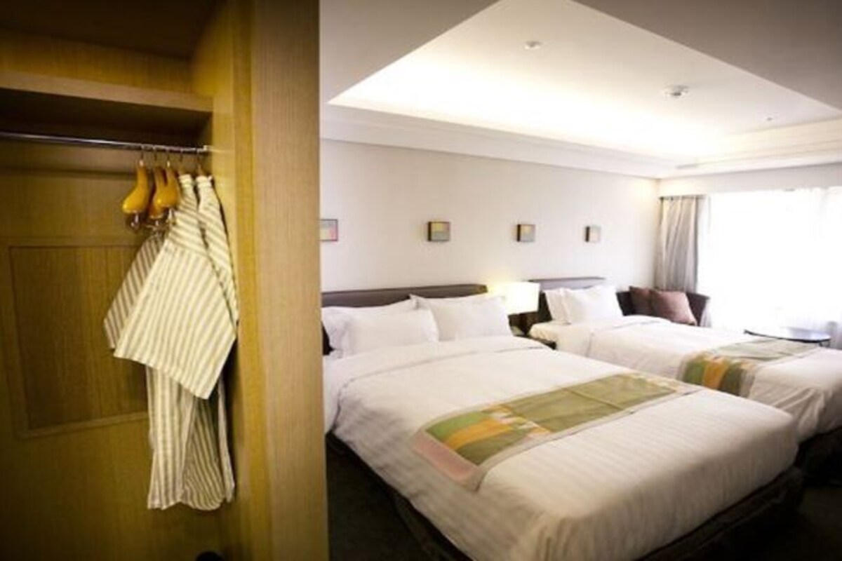 A hotel room with two beds, a wardrobe, and a window with curtains.