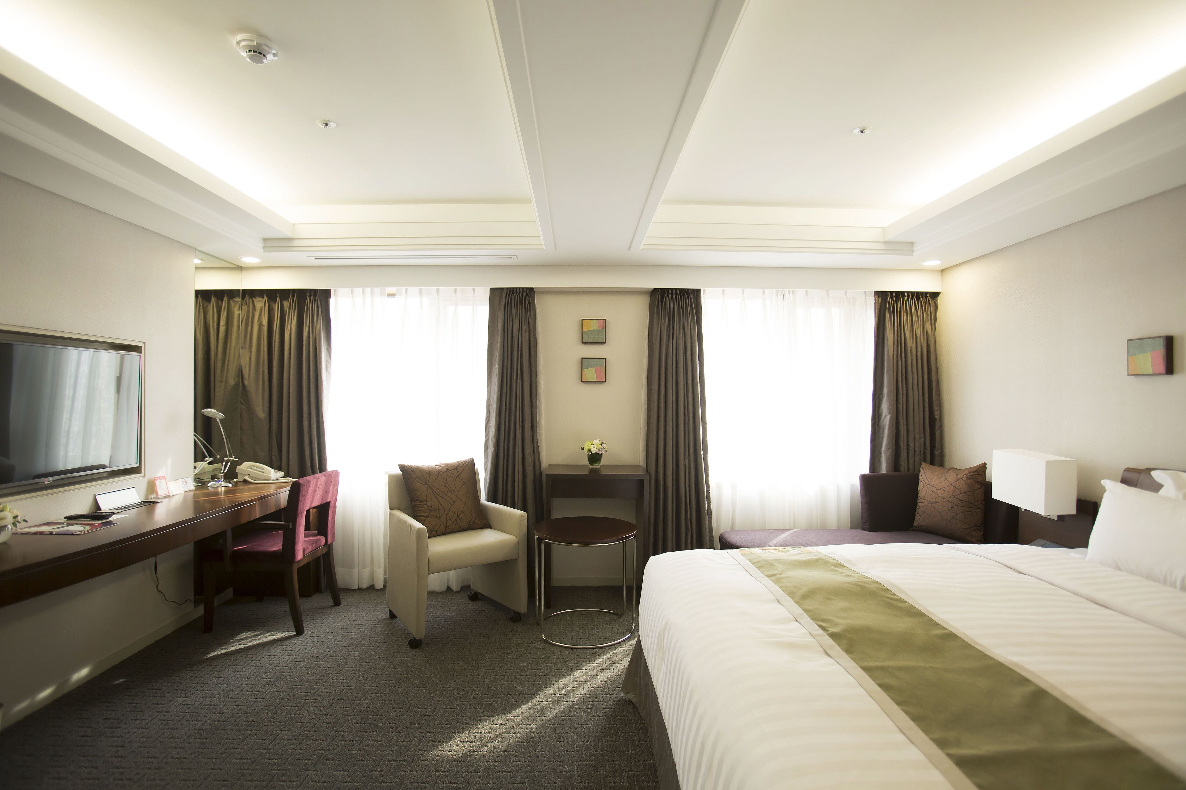 Habitación de hotel con cama, escritorio, silla, televisor y cortinas.