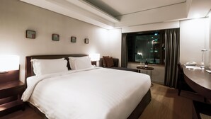 Habitación de hotel con una cama grande, un escritorio, una silla, una mesita y una ventana con cortinas.