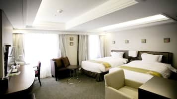 A hotel room with two beds, a desk, a chair, and a small table.