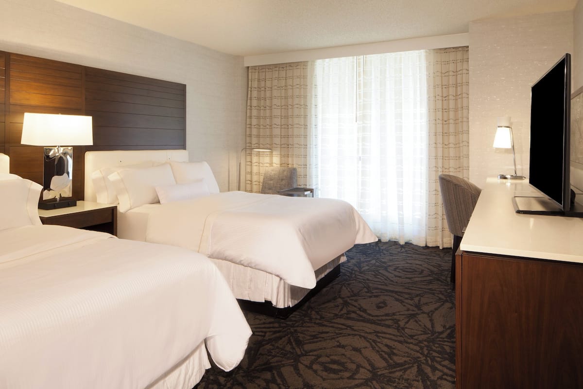 A hotel room with two beds, a desk, a chair, and a TV.